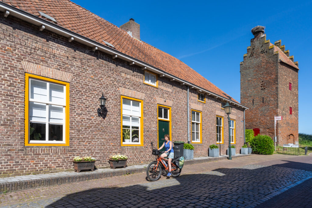 Fietser (Jessica) in Megen, met op de achtergrond de Gevangentoren, met trapgevel en ooievaarsnet